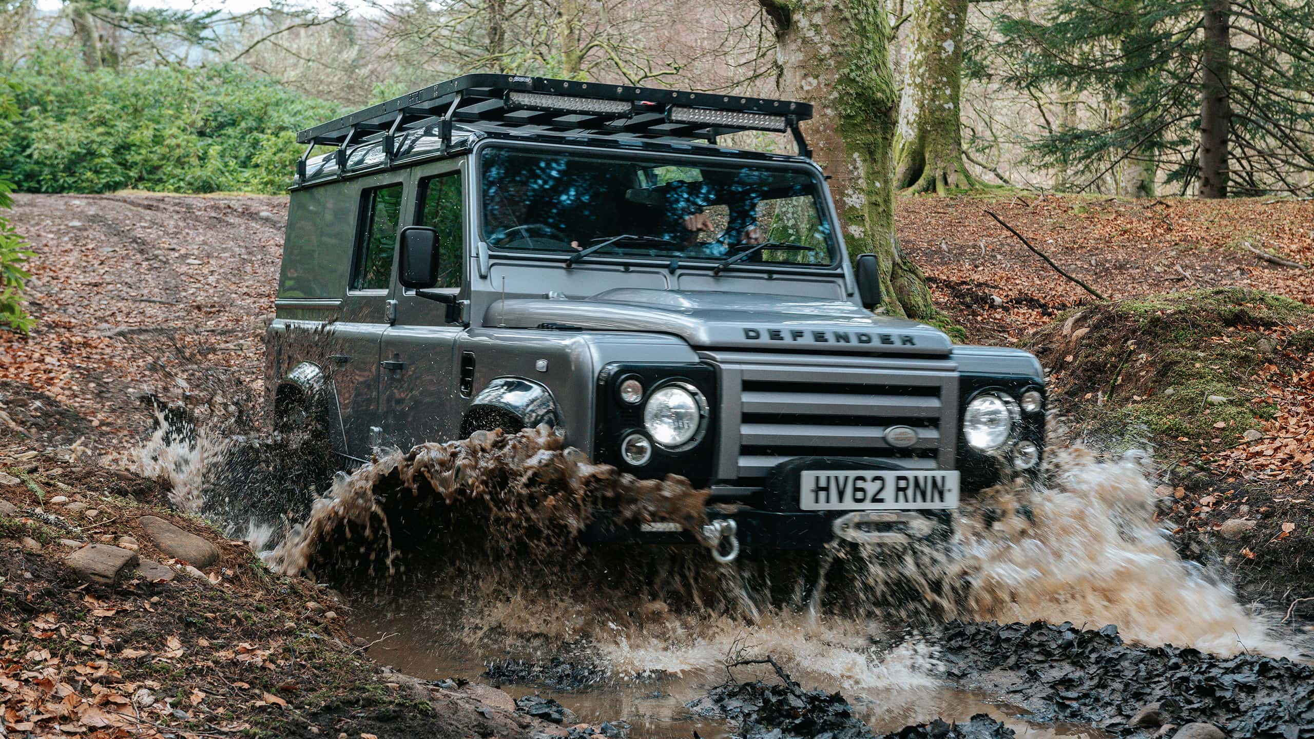 Defender driving through a muddy water crossing in a forest.